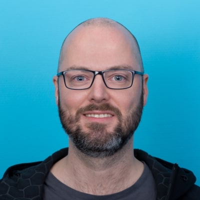 Portr&auml;t von Christian Meyer, der in die Kamera blickt und dabei l&auml;chelt; vor einem hellblauen Hintergrund.