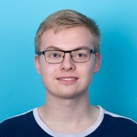 Portr&auml;t von Domenic Bartels, der in die Kamera blickt und dabei l&auml;chelt; vor einem hellblauen Hintergrund.